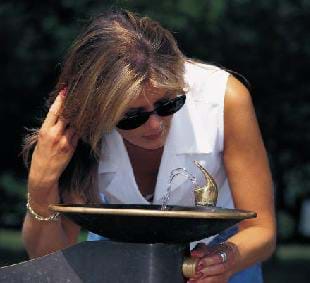 A picture of a woman drinking water from a fountain.